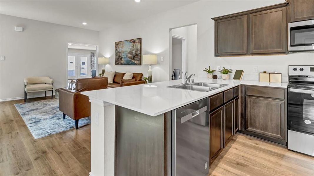 Kitchen featuring open floor plan, stainless steel appliances, dark wood finish cabinets, a peninsula, and light wood-style floors Kitchen featuring open floor plan, stainless steel appliances, dark wood finish cabinets, a peninsula, and light wood-style floors