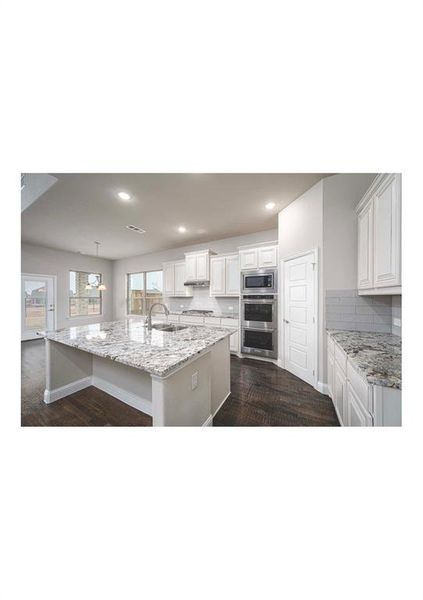 Kitchen with a large island with sink, white cabinetry, stainless steel microwave, and pendant lighting