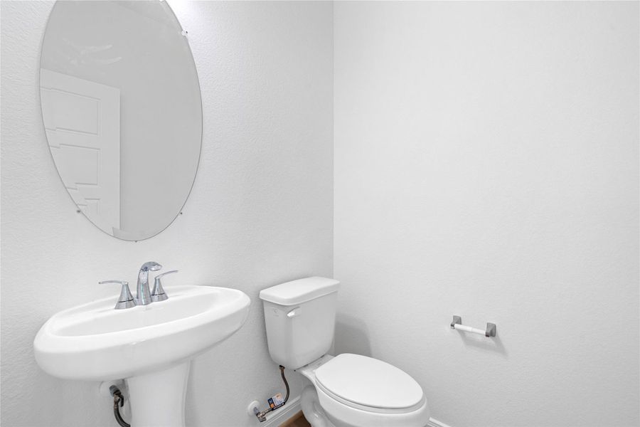 The powder room on the first floor includes a pedestal sink, oval mirror, and toilet to conveniently meet your needs.
