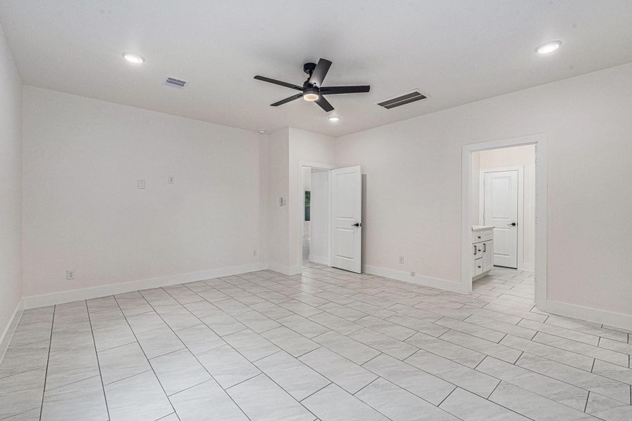 This spacious room features sleek tile flooring, neutral walls, recessed lighting, and a modern ceiling fan. It opens to an adjacent room with additional cabinetry, perfect for versatile use.