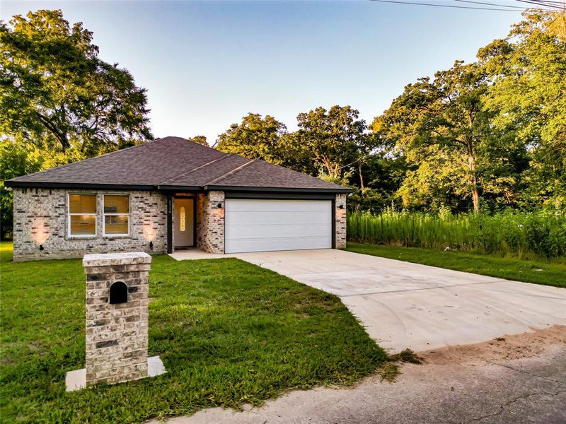 Single story home with concrete driveway, an attached garage, a shingled roof, brick siding, and a front lawn Single story home with concrete driveway, an attached garage, a shingled roof, brick siding, and a front lawn