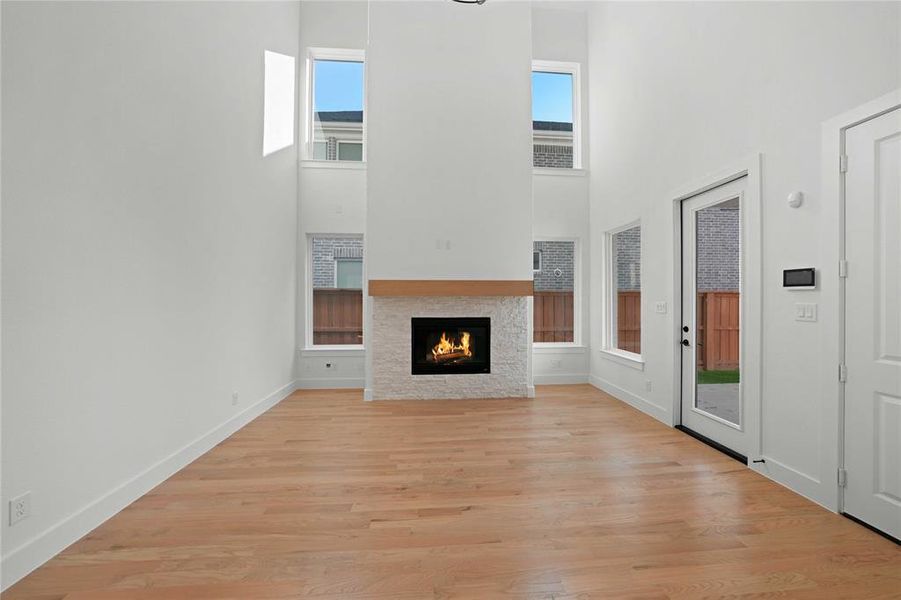 Unfurnished living room with light wood-style floors, a towering ceiling, and a warm lit fireplace Unfurnished living room with light wood-style floors, a towering ceiling, and a warm lit fireplace