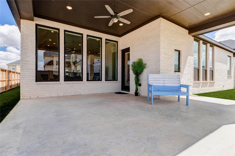 This photo showcases a spacious covered patio with a ceiling fan, perfect for outdoor relaxation. It features large windows that provide ample natural light, a light brick exterior, and a neatly maintained lawn, creating an inviting outdoor living space. This photo showcases a spacious covered patio with a ceiling fan, perfect for outdoor relaxation. It features large windows that provide ample natural light, a light brick exterior, and a neatly maintained lawn, creating an inviting outdoor living space.