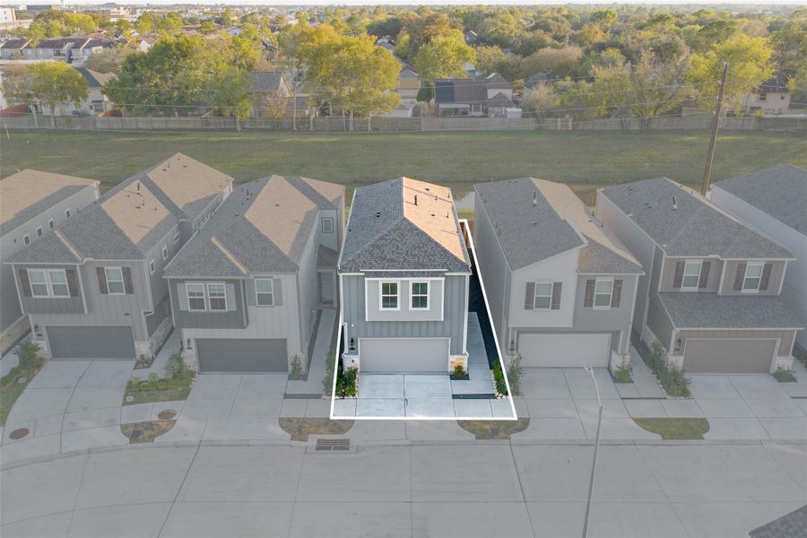 This photo showcases a modern two-story home with a gray exterior and a small front yard. It features a double garage and is situated in a neat, suburban neighborhood with similar homes. The property backs onto a green space, offering added privacy and a pleasant view.