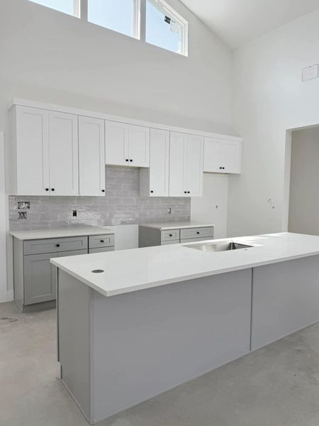 backsplash, a high ceiling, gray cabinets, and concrete floors