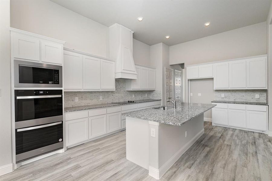 Kitchen featuring white cabinets, light stone counters, a center island with sink, and black cooktop