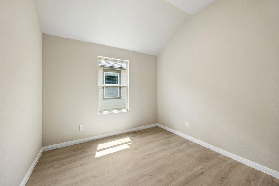 A well-lit bedroom features vaulted ceilings and light wood flooring.