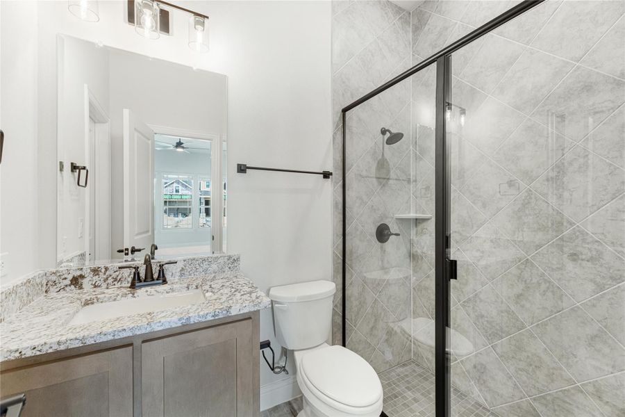 Bathroom with granite vanity, walk-in glass shower with gray tile, and black fixtures