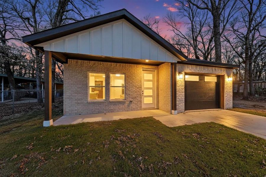 View of front facade featuring board and batten siding, driveway, brick siding, and an attached garage