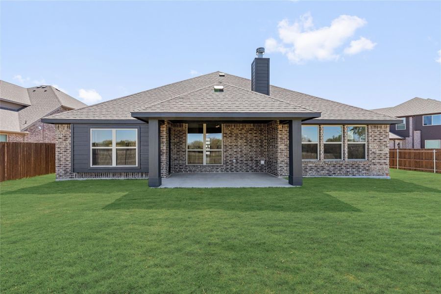 Rear exterior of single-story brick home with covered patio, chimney, and fenced backyard lawn