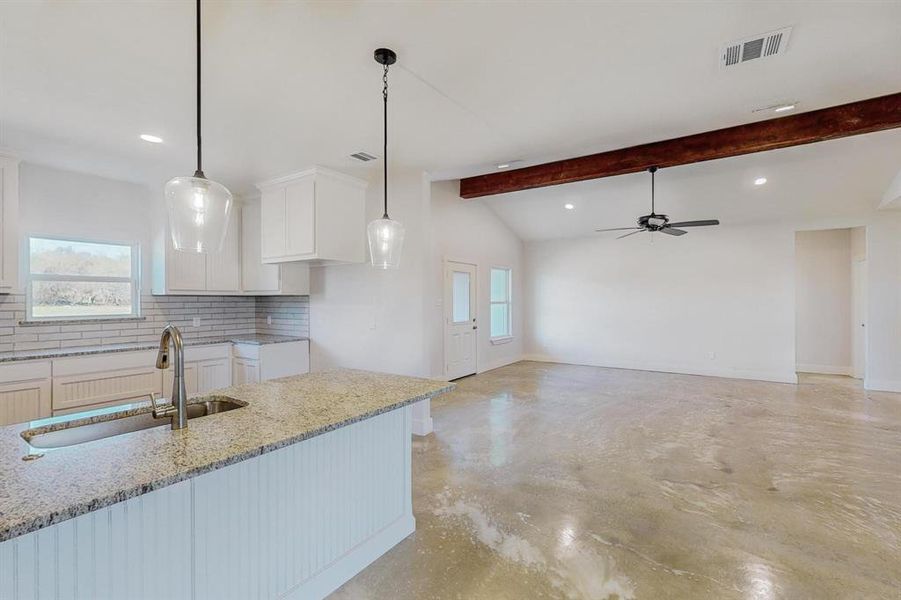 Kitchen with decorative backsplash, sink, vaulted ceiling with beams, white cabinetry, and hanging light fixtures