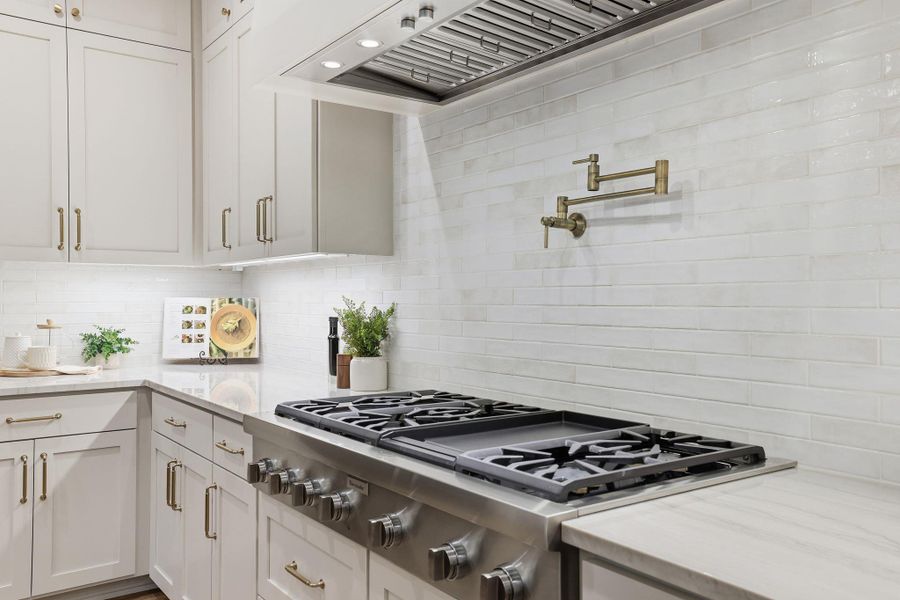 Kitchen featuring stainless steel gas cooktop, custom exhaust hood, light stone counters, white cabinetry, and decorative backsplash