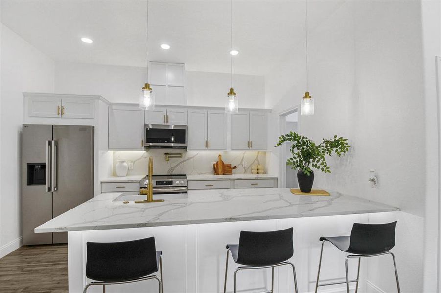 Kitchen featuring a kitchen bar, decorative backsplash, stainless steel appliances, a peninsula, and light stone counters Kitchen featuring a kitchen bar, decorative backsplash, stainless steel appliances, a peninsula, and light stone counters