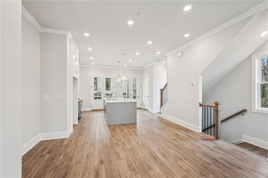 Kitchen featuring a center island with sink, pendant lighting, light wood-style flooring, crown molding, and white cabinetry