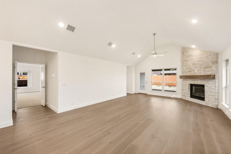 Open living room with vaulted ceiling, hardwood floors, and stone fireplace with wood mantel Open living room with vaulted ceiling, hardwood floors, and stone fireplace with wood mantel