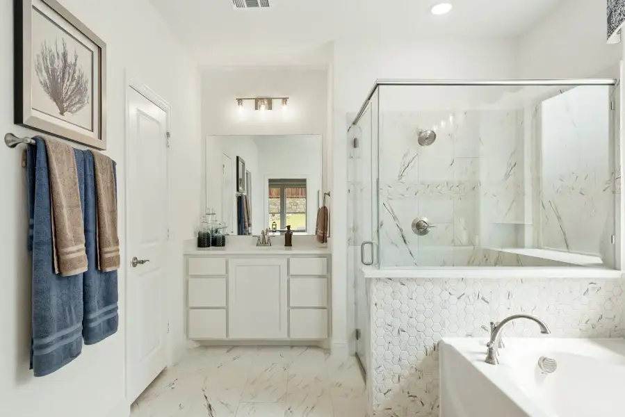 Bathroom with white vanity, glass-enclosed shower, soaking tub, and marble tile floors and walls