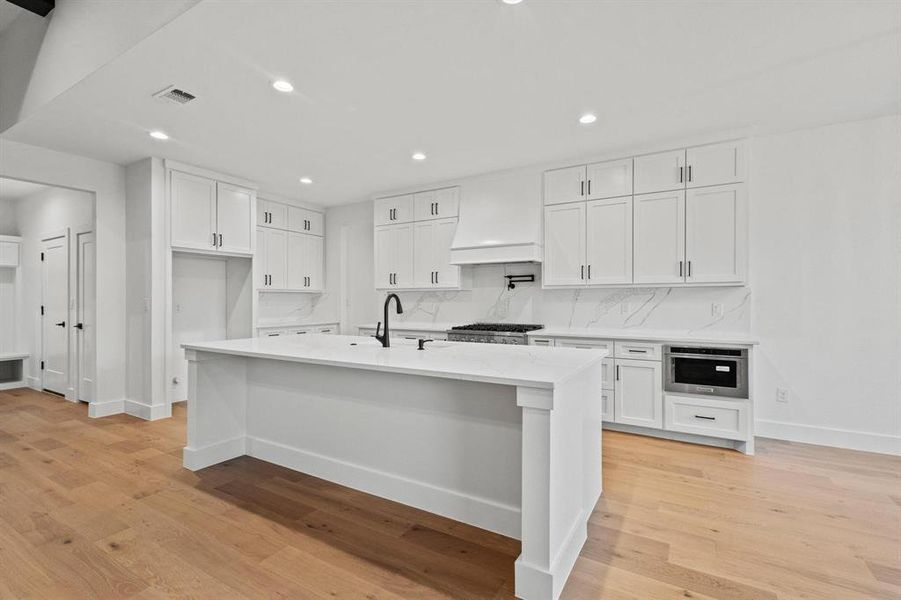 Kitchen featuring white cabinetry, recessed lighting, a kitchen bar, decorative backsplash, and light stone countertops