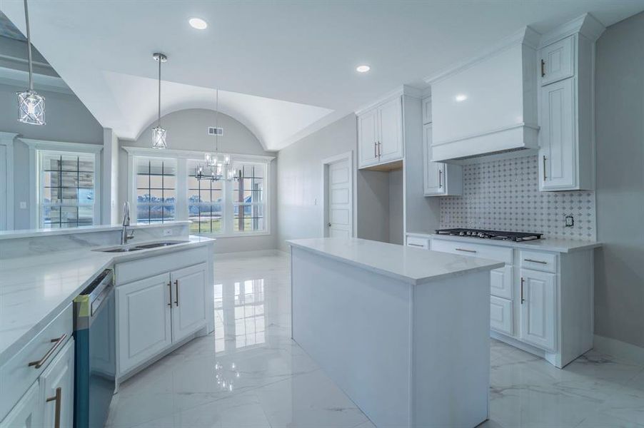 Kitchen featuring light stone counters, dishwasher, white cabinets, a kitchen island, and vaulted ceiling