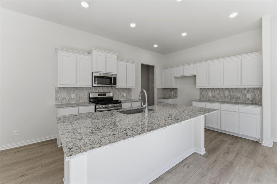 Kitchen featuring white cabinets, light stone counters, stainless steel appliances, backsplash, and light wood-style floors