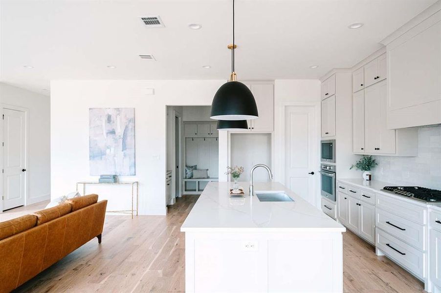 Kitchen with sink, decorative light fixtures, tasteful backsplash, an island with sink, and appliances with stainless steel finishes