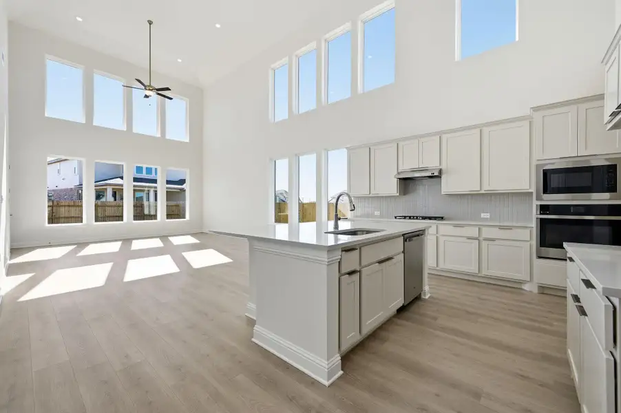 Kitchen with stainless steel appliances, open floor plan, white cabinets, backsplash, and a high ceiling