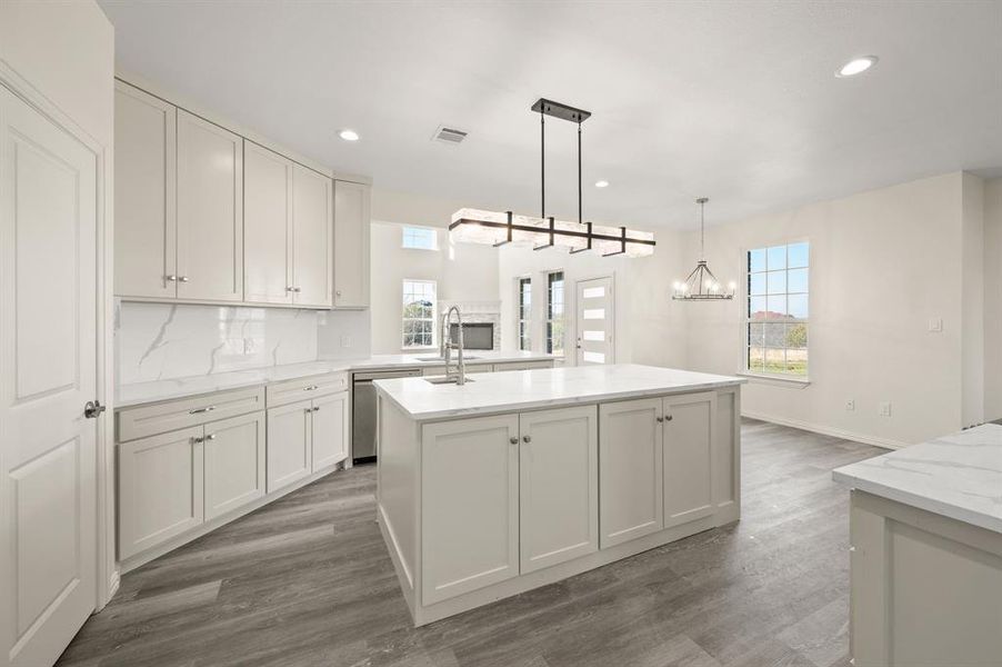 Kitchen with decorative light fixtures, wood finished floors, decorative backsplash, a center island with sink, and recessed lighting Kitchen with decorative light fixtures, wood finished floors, decorative backsplash, a center island with sink, and recessed lighting