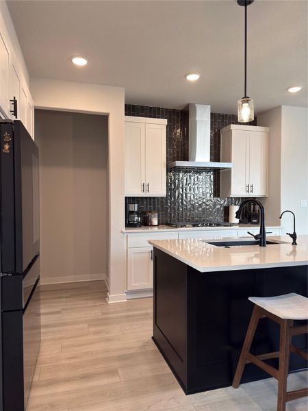 Modern kitchen featuring a dark tile backsplash, light wood-finish flooring, white cabinetry, and a dark kitchen island with a light countertop