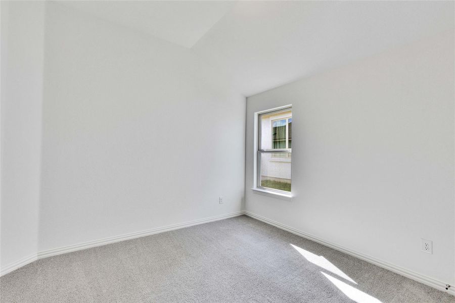 Carpeted empty room featuring vaulted ceiling and baseboards Carpeted empty room featuring vaulted ceiling and baseboards