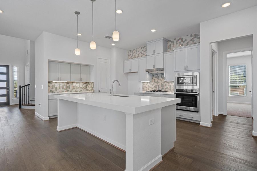 Kitchen featuring healthy amount of natural light, decorative backsplash, dark wood-style floors, and an island with sink Kitchen featuring healthy amount of natural light, decorative backsplash, dark wood-style floors, and an island with sink