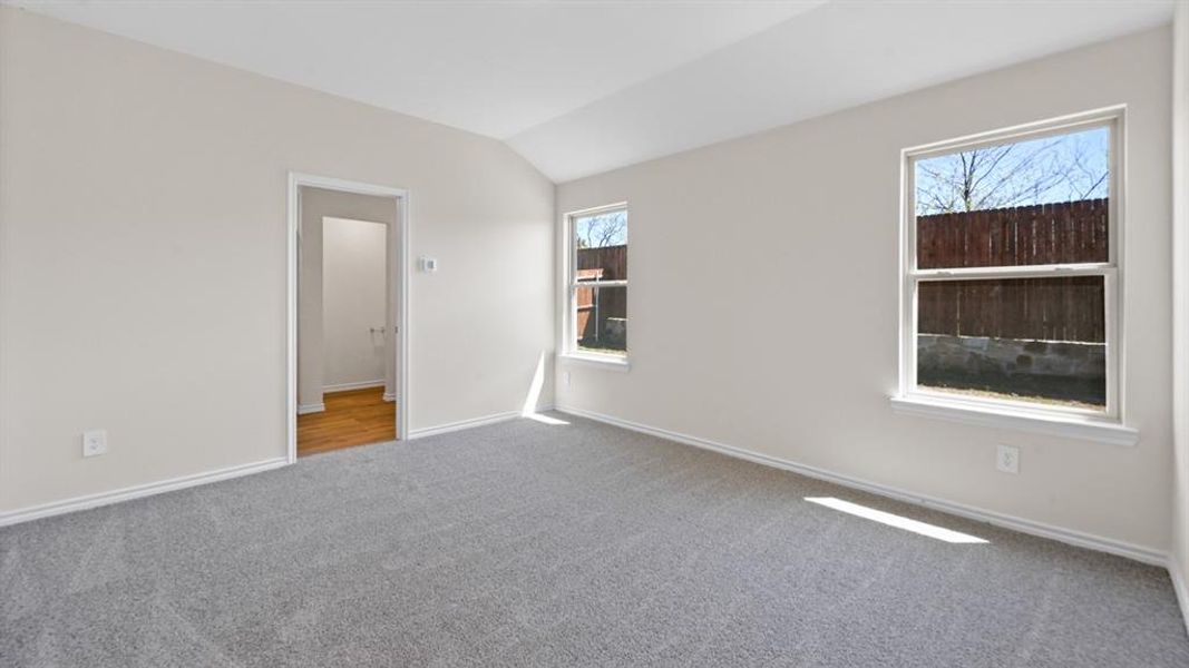 Spacious room featuring vaulted ceilings, light gray wall paint, and plush gray carpeting