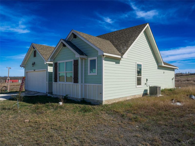 View of side of home featuring roof with shingles, a garage, and a yard