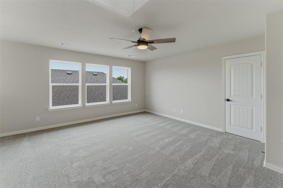 Spacious room featuring light gray carpet, multiple windows, a ceiling fan, and a paneled white door with dark hardware
