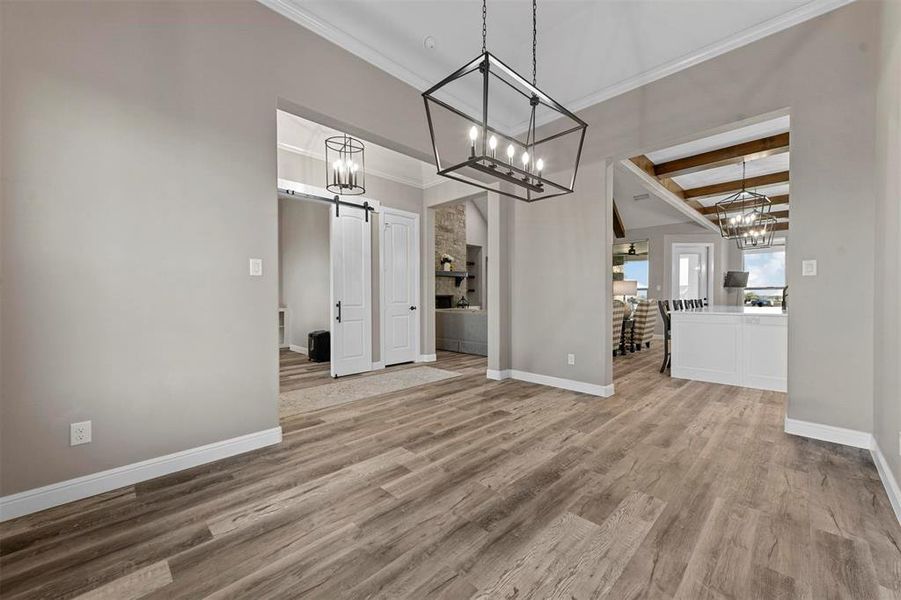 Unfurnished dining area with beamed ceiling, a barn door, hardwood / wood-style flooring, and ornamental molding