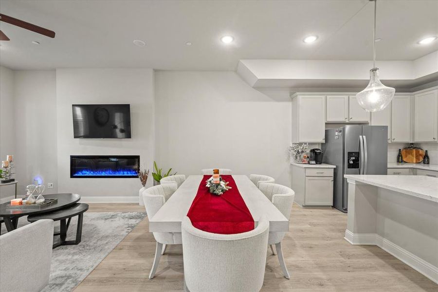 Kitchen with white cabinetry, light wood-type flooring, decorative light fixtures, stainless steel fridge, and a kitchen breakfast bar