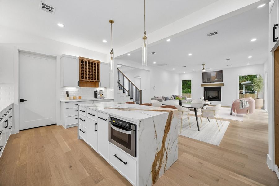 Positioned at the center of the home, the kitchen maintains direct connection to the surrounding living and dining spaces while balancing clean contemporary finishes with everyday functionality. The layout was designed to feel open without sacrificing workspace, combining natural light, extensive cabinetry, designer lighting, and a large center island within the heart of the main level. (digitally staged)