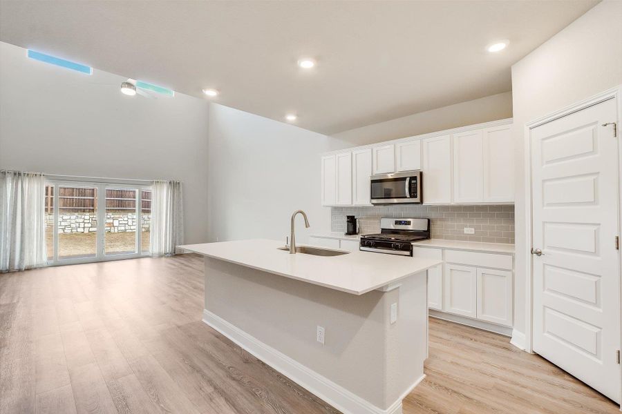 Kitchen with a sink, light wood-style floors, appliances with stainless steel finishes, decorative backsplash, and an island with sink