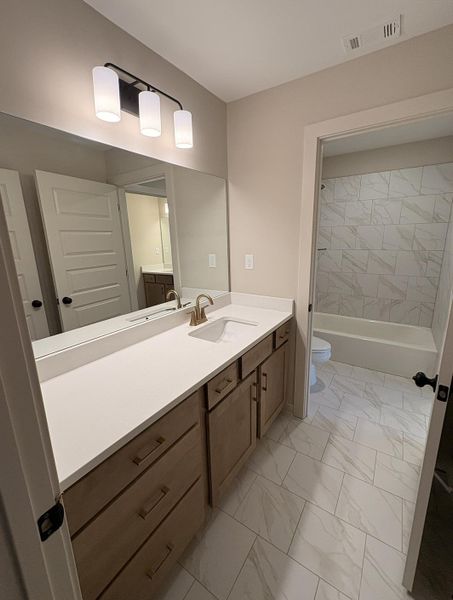 Bathroom vanity featuring light wood-finish cabinetry, a single undermount sink, and a white countertop