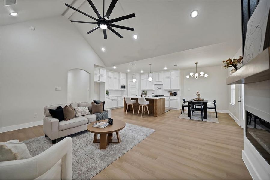 Living area featuring light wood-style floors, recessed lighting, high vaulted ceiling, a ceiling fan, and a large fireplace Living area featuring light wood-style floors, recessed lighting, high vaulted ceiling, a ceiling fan, and a large fireplace
