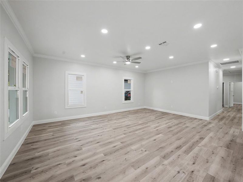Spacious room featuring wood-finish flooring, recessed lighting, a ceiling fan, crown molding, and multiple windows
