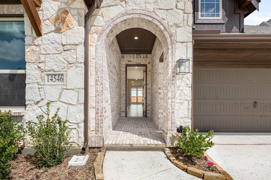Stone and brick arched entryway with covered walkway leading to front door and attached garage Stone and brick arched entryway with covered walkway leading to front door and attached garage