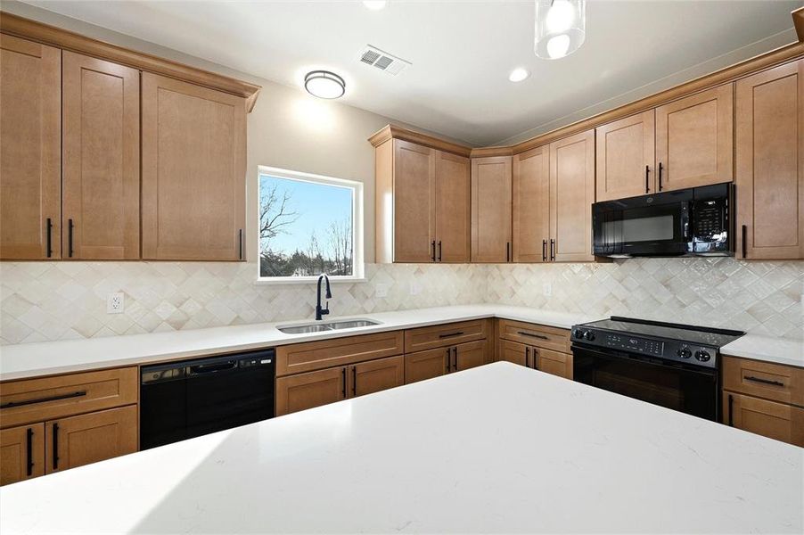 Kitchen with black appliances, wood finish cabinets, light stone counters, backsplash, and recessed lighting Kitchen with black appliances, wood finish cabinets, light stone counters, backsplash, and recessed lighting