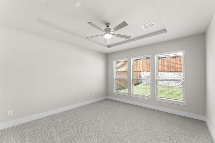 Spacious room featuring light-toned carpeting, a tray ceiling with a modern ceiling fan, and three large windows Spacious room featuring light-toned carpeting, a tray ceiling with a modern ceiling fan, and three large windows