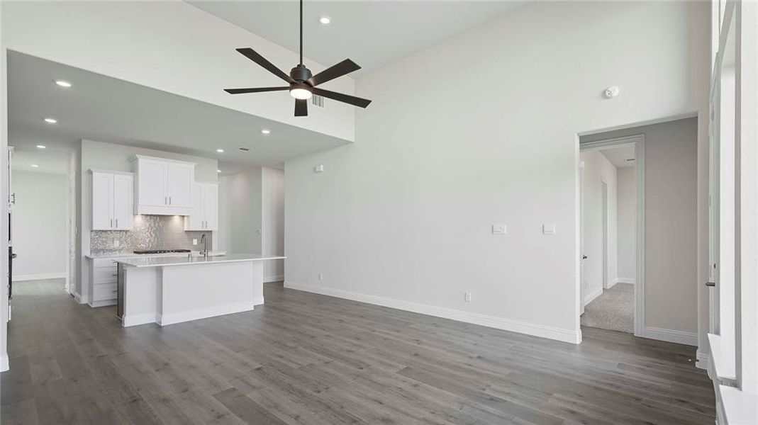 Spacious open concept room featuring wood-finish flooring, a contemporary ceiling fan, and a kitchen area with white cabinetry, a large island, and a textured backsplash