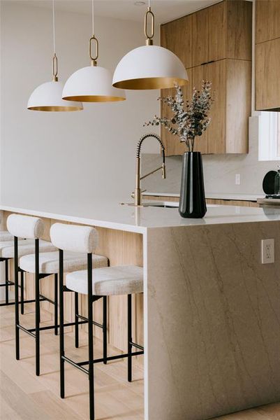 Kitchen with sink, a kitchen bar, light hardwood / wood-style floors, and decorative light fixtures