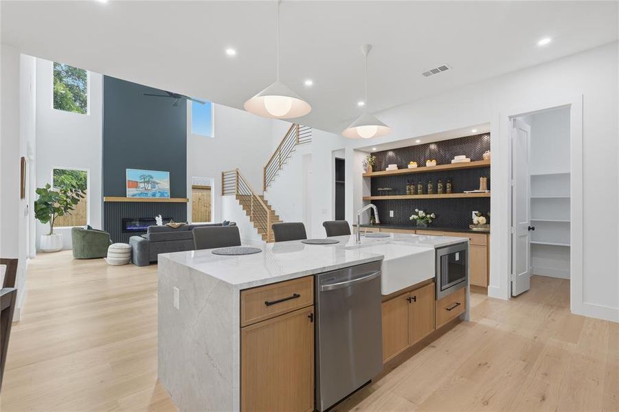 Open-concept kitchen featuring a waterfall island with a farmhouse sink, stainless steel appliances, and a built-in microwave Open-concept kitchen featuring a waterfall island with a farmhouse sink, stainless steel appliances, and a built-in microwave