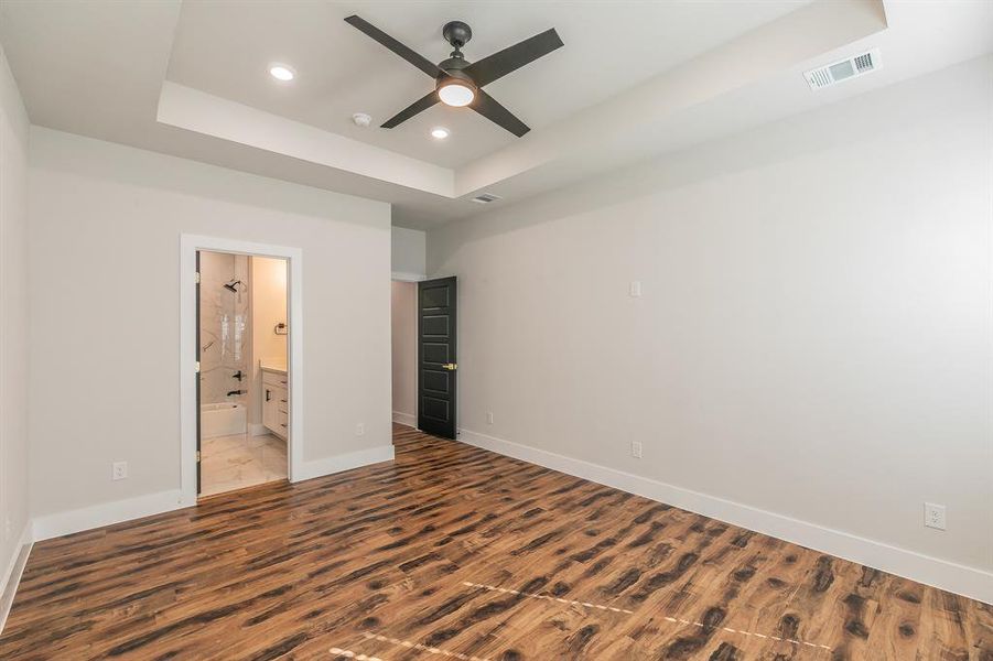 Unfurnished bedroom featuring a tray ceiling, connected bathroom, ceiling fan, and light hardwood / wood-style flooring