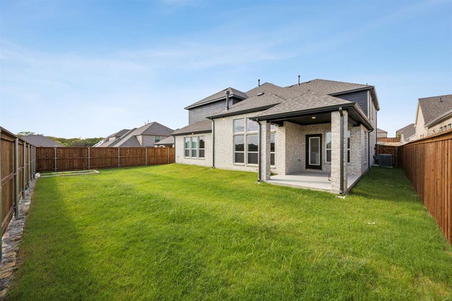 Back of property with cooling unit, a lawn, and a patio