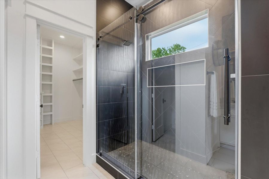 The shower features three showerheads including a rain head, overhead, and handheld, along with an oversized niche, penny tile flooring, a sliding glass door, and a window for beautiful natural light.