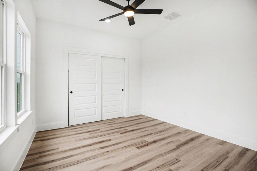 Bright and airy room with large windows, modern ceiling fan, wood-style flooring, and a double sliding door closet. Perfect for a bedroom or home office.