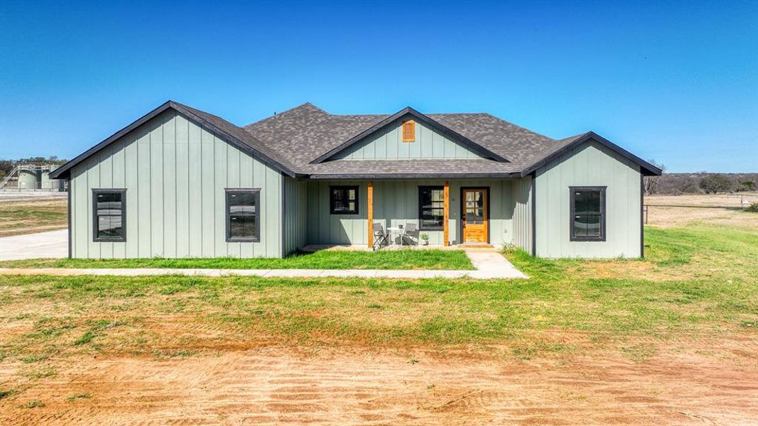 Modern farmhouse with roof with shingles, a front yard, a porch, and board and batten siding